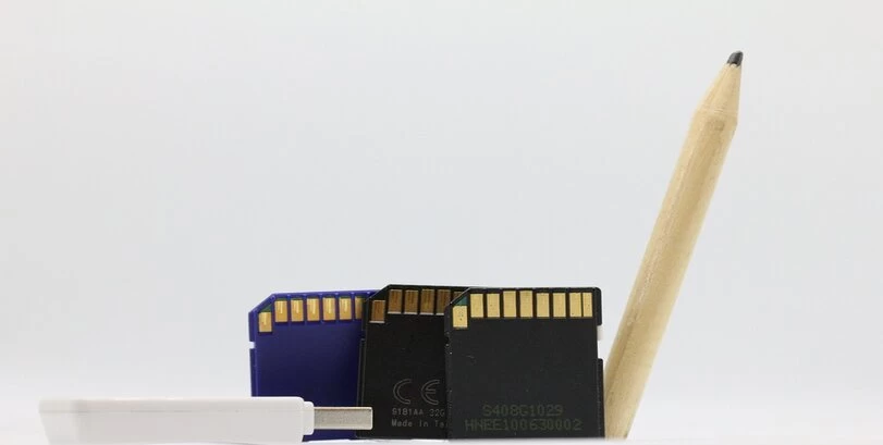 An image of 3 SD cards, a USB stick, and a pencil on a white background.